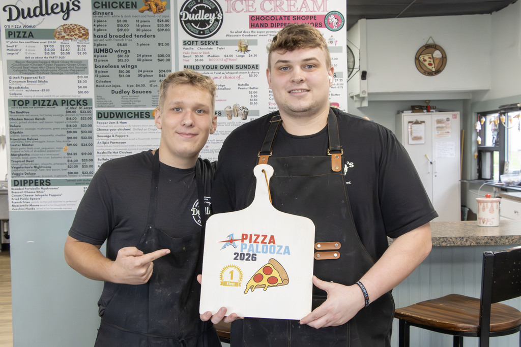 Two young men in aprons hold a pizza peel as the award for pizza palooza