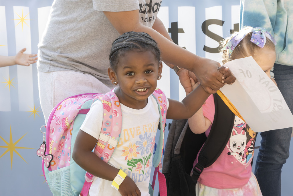 A student smiling with a backpack on while holding her mothers hand