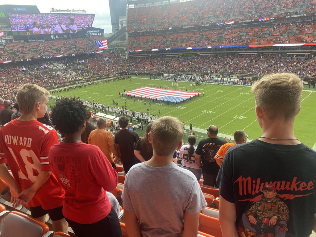 Four students standing as a flag is displayed on the Cleveland Browns Football field