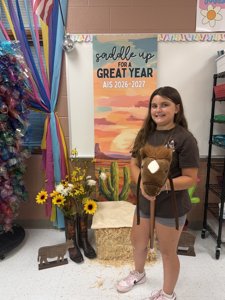 Two students sitting in front of a "Saddle Up for a great year AIS" banner