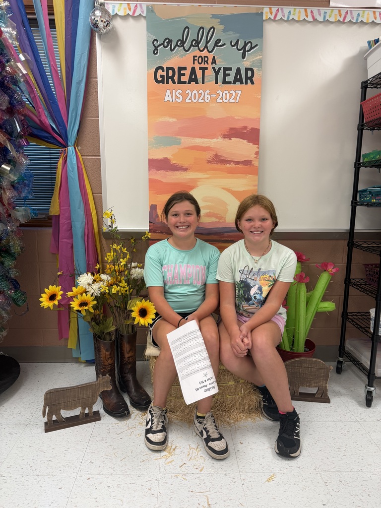 Two students sitting in front of a "Saddle Up for a great year AIS" banner