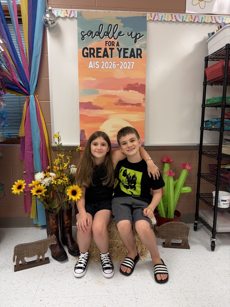 Two students sitting in front of a "Saddle Up for a great year AIS" banner