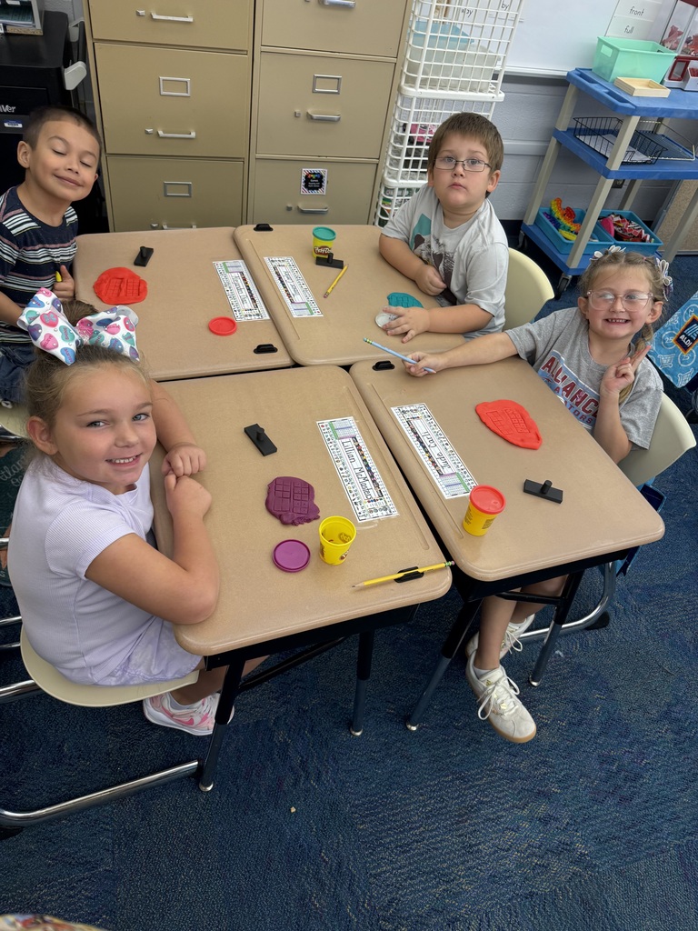 Elementary students use colorful Play-Doh and ten-frame grids to practice counting during a classroom center activity.