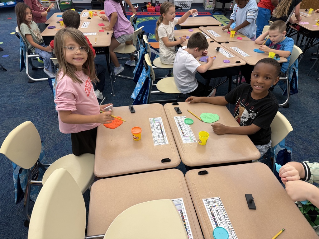 Elementary students use colorful Play-Doh and ten-frame grids to practice counting during a classroom center activity.