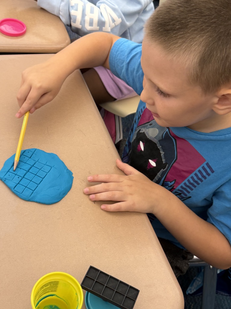 Elementary students use colorful Play-Doh and ten-frame grids to practice counting during a classroom center activity.