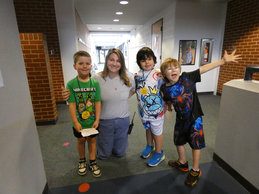 Three students smiling while an adult kneels down to take a picture with them