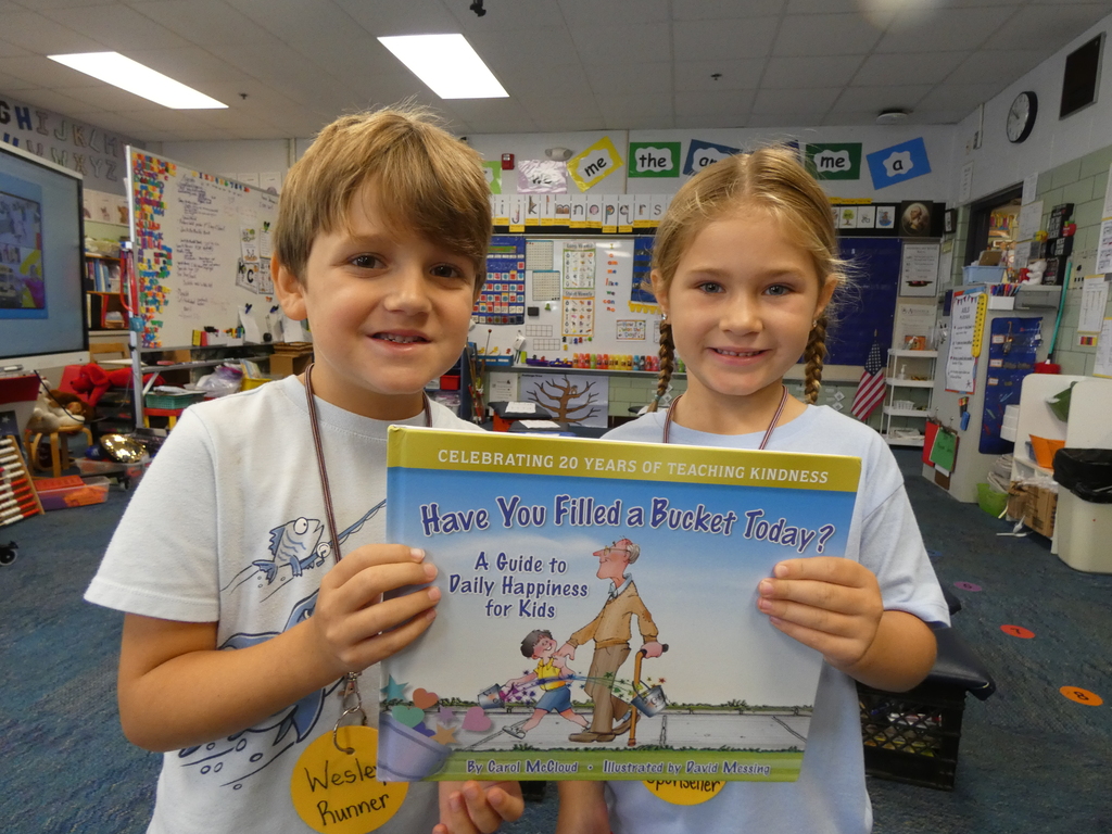 Two students smile while holding up the book "Have you filled a bucket today?"
