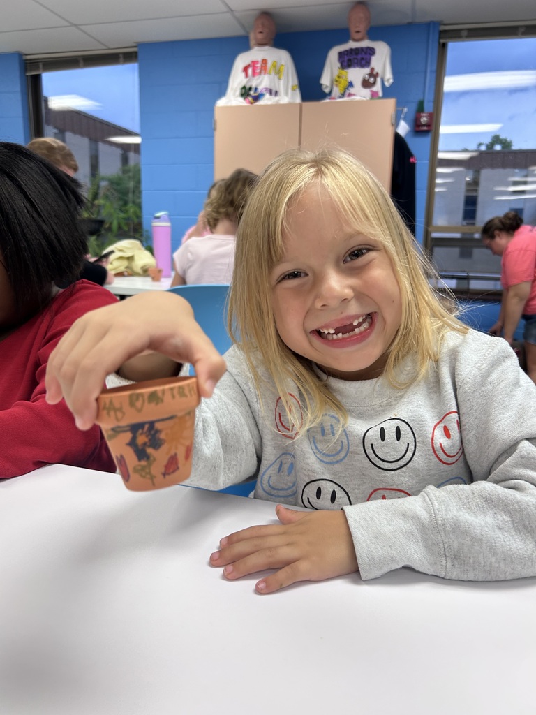A student smiling while holding the clay pot she decorated