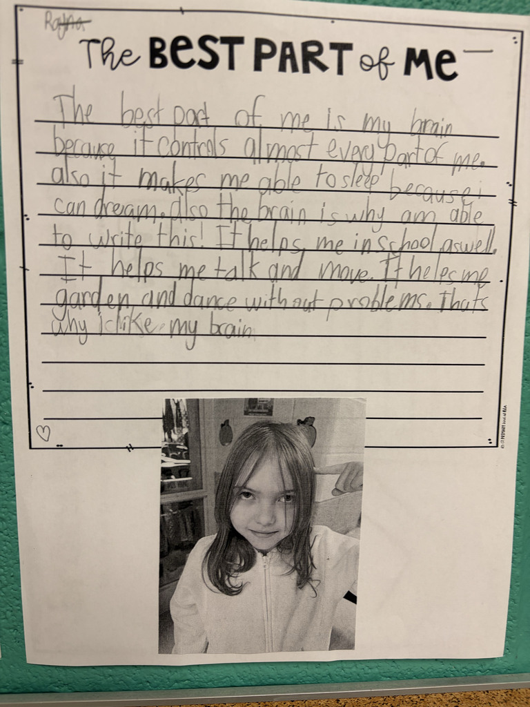A student worksheet titled “The Best Part of Me” is displayed on a classroom wall. The student wrote about why their brain is the best part of them. A black-and-white photo of the student is attached at the bottom of the page.  The student’s writing reads: “The best part of me is my brain because it controls almost every part of me. Also it makes me able to sleep because I can dream. Also the brain is why I am able to write this! It helps me in school as well. It helps me talk and move. It helps me garden and dance without problems. That’s why I like my brain.”