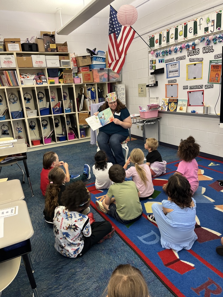 Mariah holds a book while wearing a birthday crown as the students sit around her listening to the story.