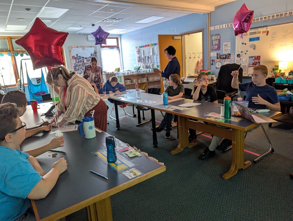Students in a classroom hold balloons and pennies while doing a science experiment