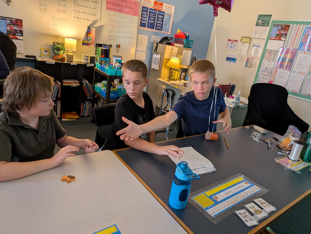 Students in a classroom hold balloons and pennies while doing a science experiment