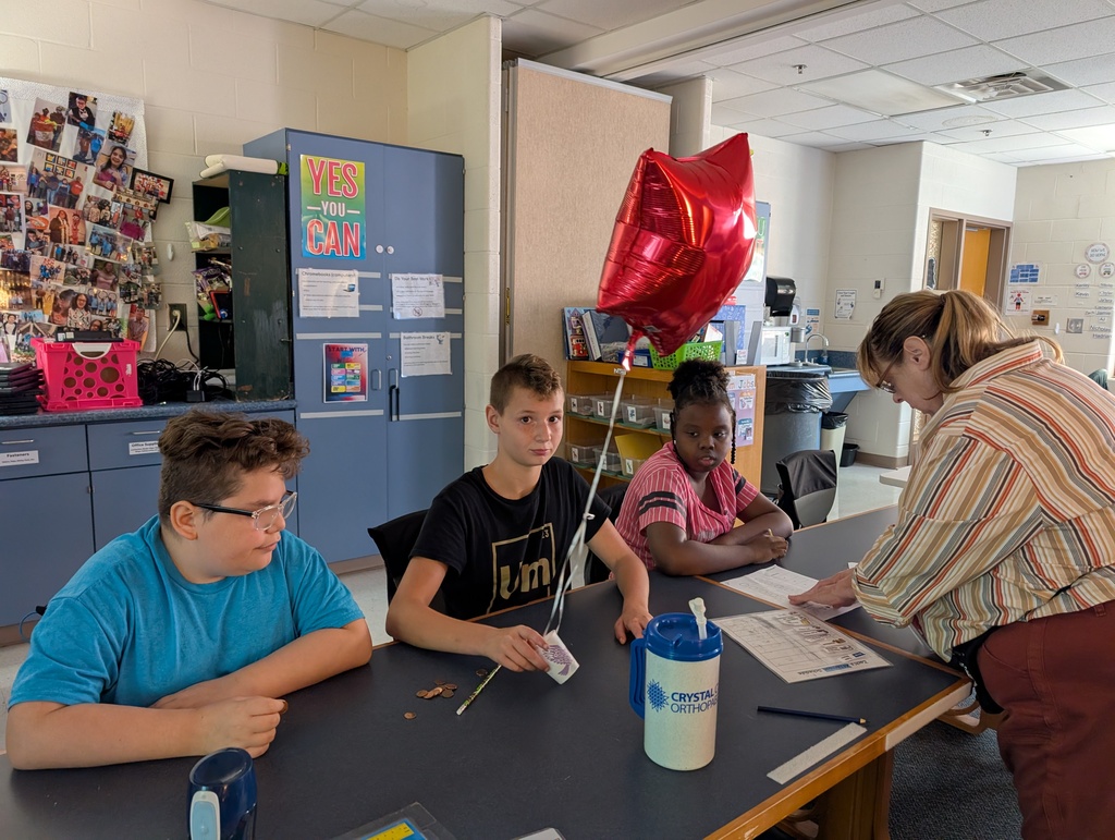 Students in a classroom hold balloons and pennies while doing a science experiment