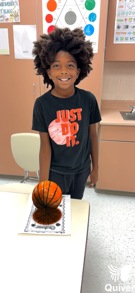 A student stands while holding what appears to be a 3-d generated sphere she used with the quiver app of the dot they created