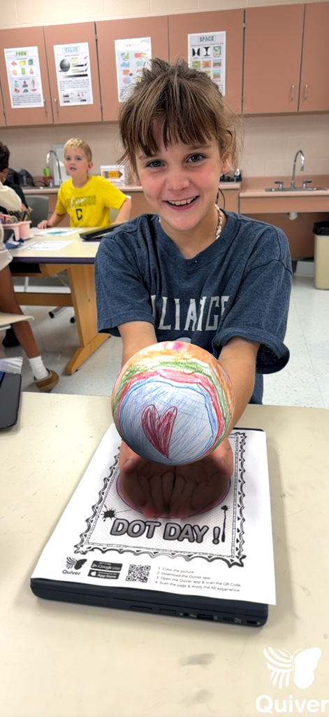 A student stands while holding what appears to be a 3-d generated sphere she used with the quiver app of the dot they created