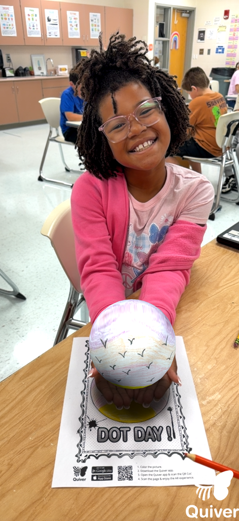 A student stands while holding what appears to be a 3-d generated sphere she used with the quiver app of the dot they created