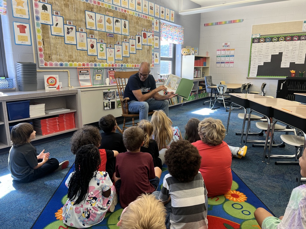 Mr. Jackson holds up a story book while students sit on a rug un front of him
