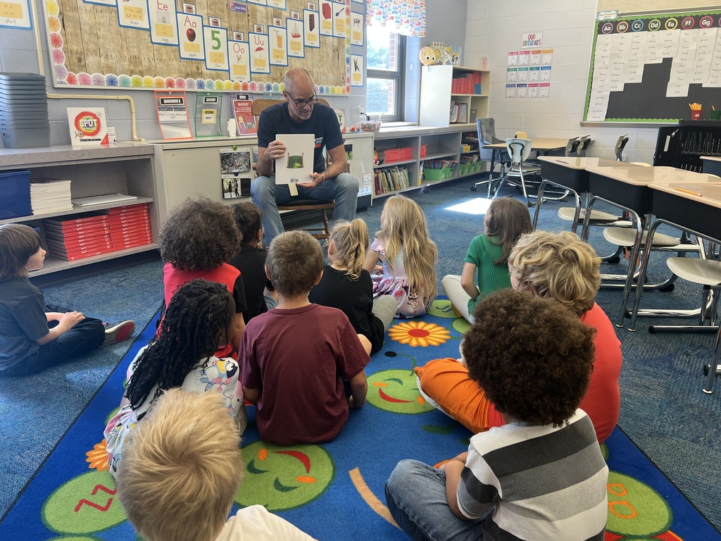Mr. Jackson holds up a story book while students sit on a rug un front of him