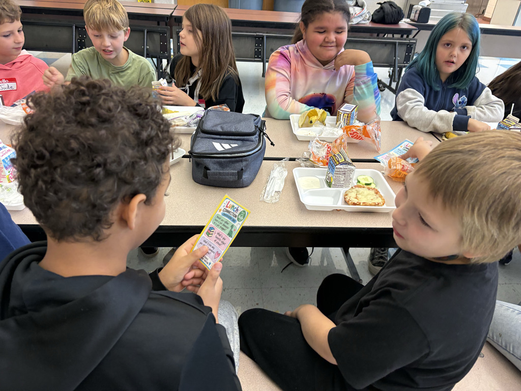 A student holds a conversation starter card while talking to another student