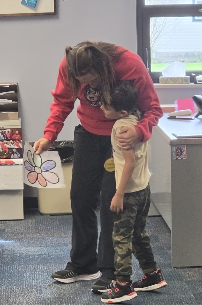 An adult holds a colored picture while hugging a student