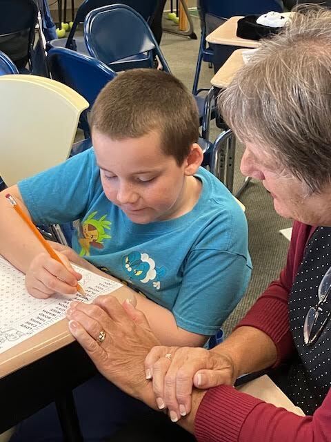 A grandmother watches while her grandson completes a word search