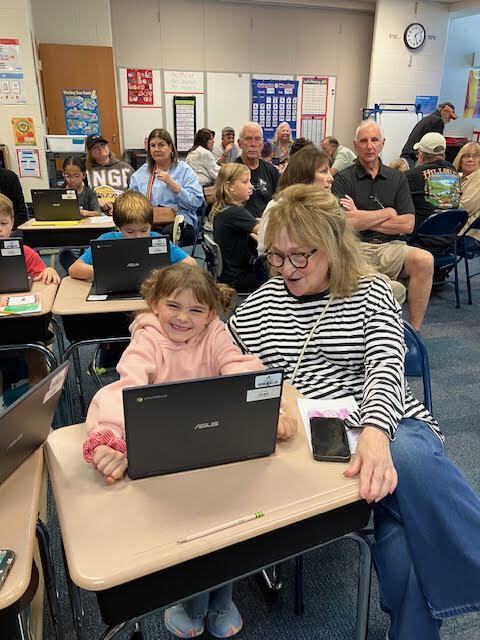 A grandmother watches while her grandchild shows her something on her chromebook