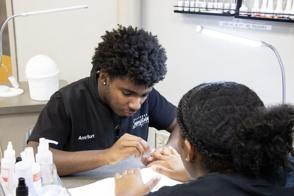 a cosmetology student giving a client a manicure at a nail station