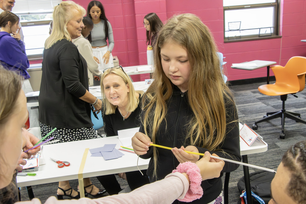 A students works to connect straws during the activity while an adult watches