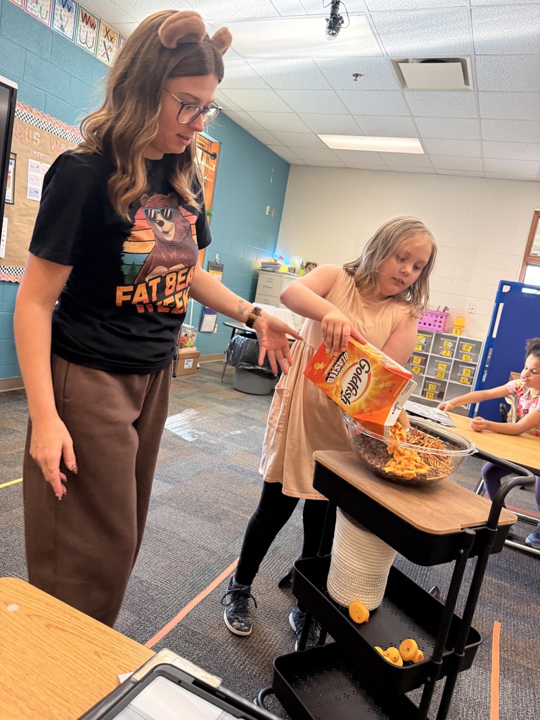 A teacher helps a student poor a bag of goldfish crackers into a bowl