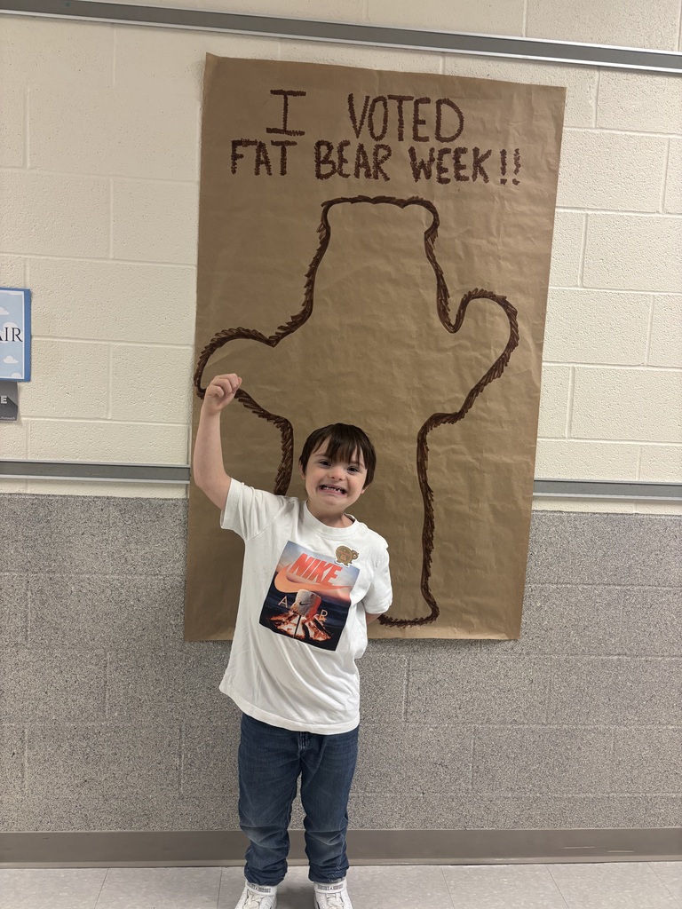 A student stands in front of a larch poster with with the outline of a bear and the words "I voted Fat Bear Week"