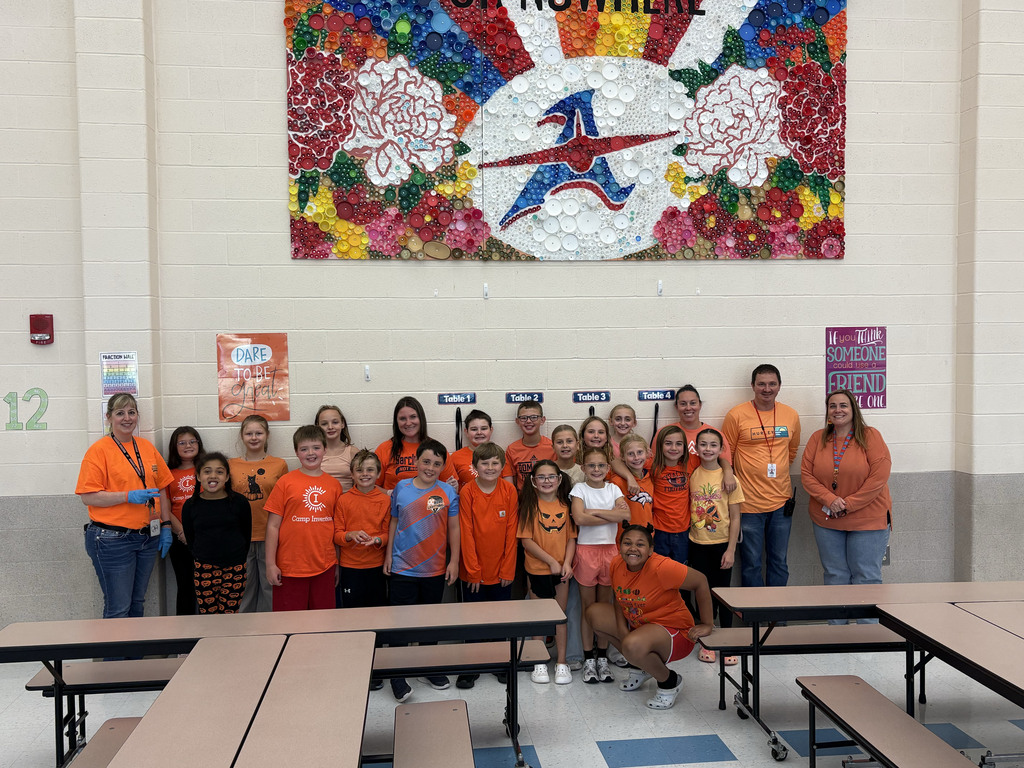 A large group of students and staff members stand together for a picture. All are wearing orange
