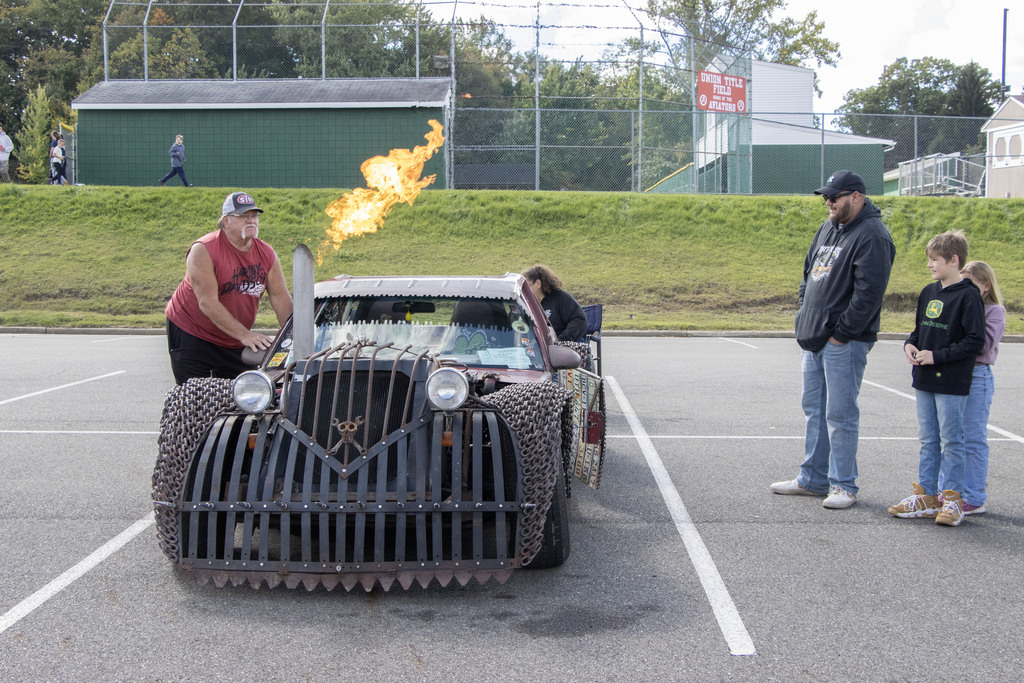 A man and two children watch as a car owner revs fire out of car