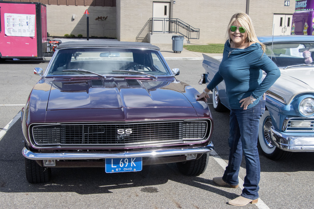 A woman stands next to a vintage purple camaro 