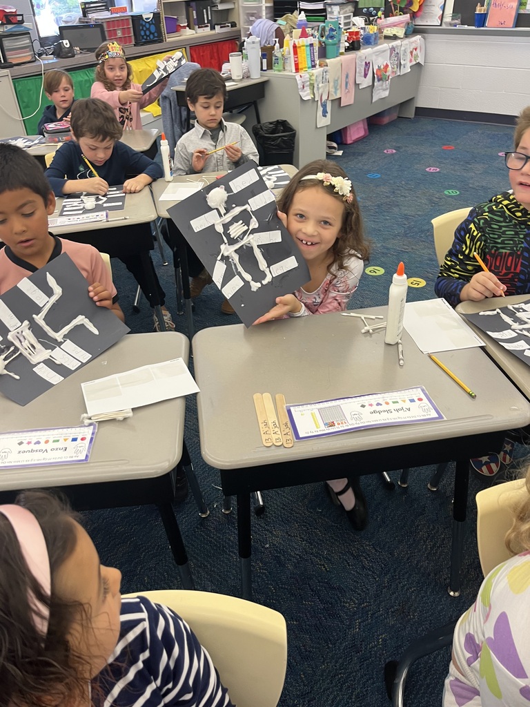A student holds up her completed skeleton diagram while other work on theirs around her