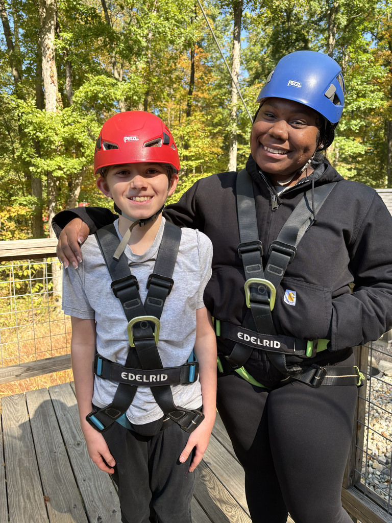 An AMS student and a high school camp counselor wear a helmet and harness while waiting for the zip line