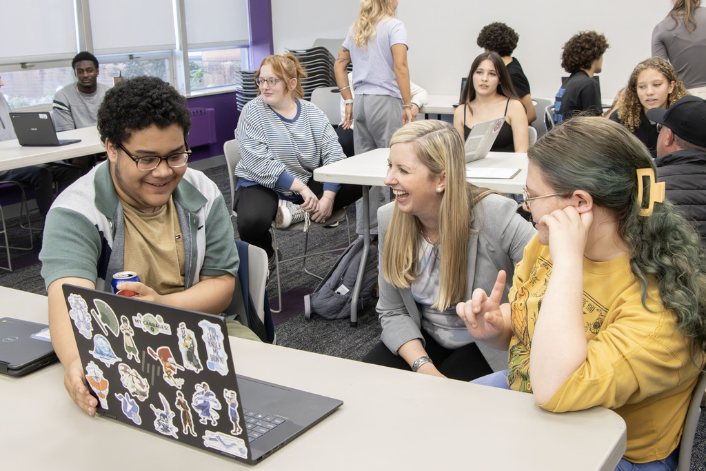 A high school student smiles while looking at his computer screen while a UMU faculty member laughs