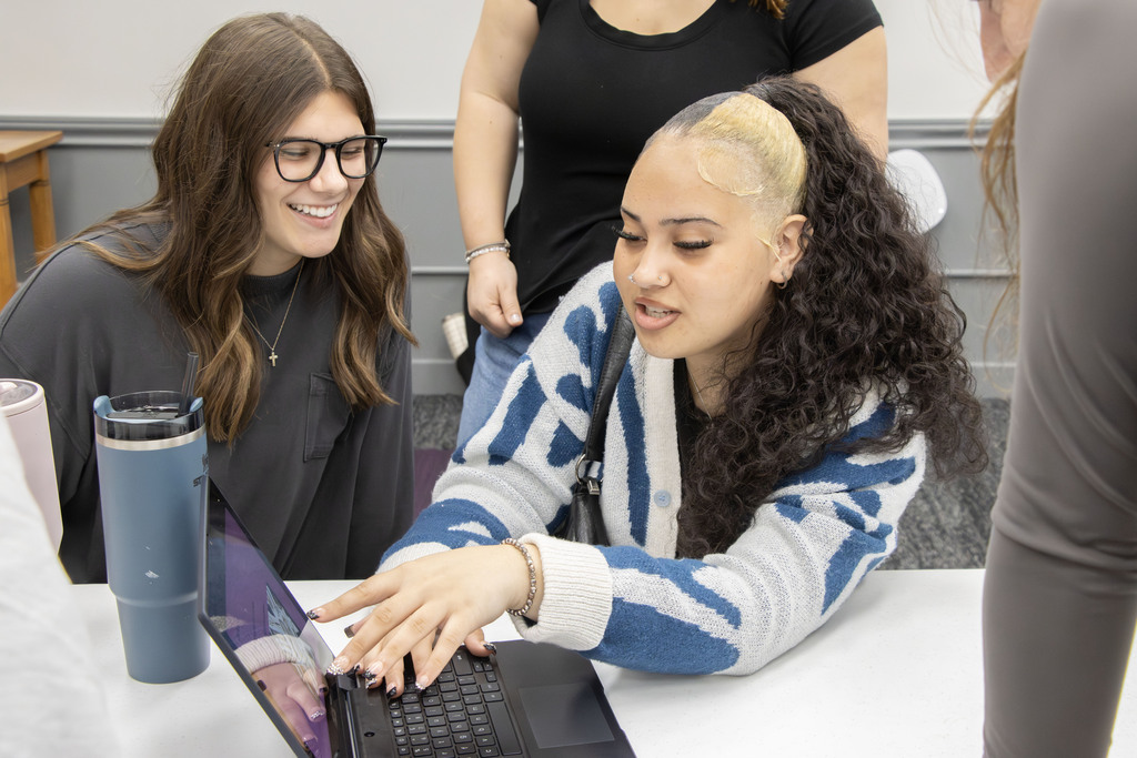 An AHS student points to her computer screen while a UMU student smiles beside her.