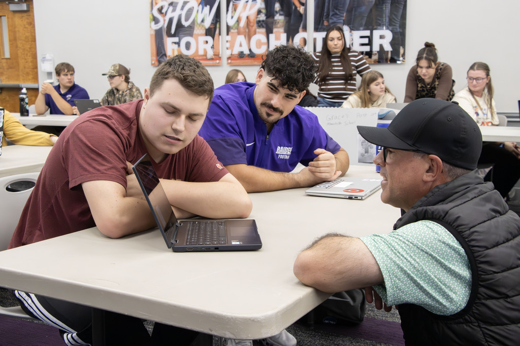 An AHS student, a UMU student and a UMU faculty member look at a screen while the student presents his presentation