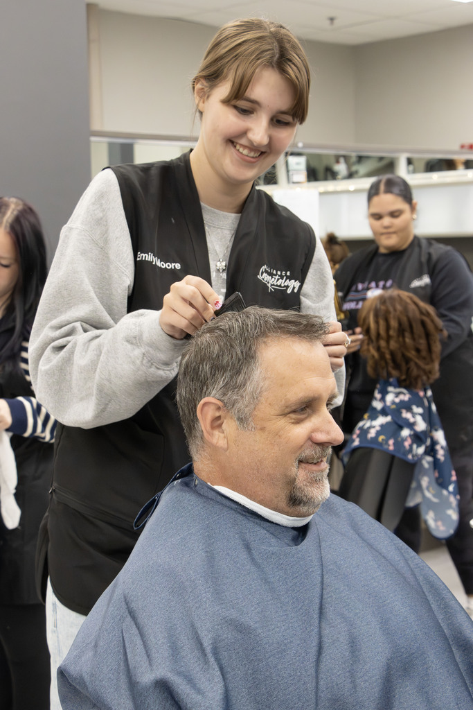Mr. Gress smiles and talks to emily while she smiles and cuts his hair.