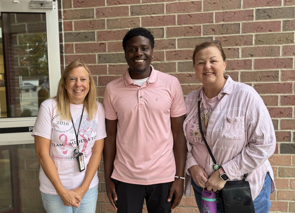 Three staff members smile for a picture. All are wearing pink shirts