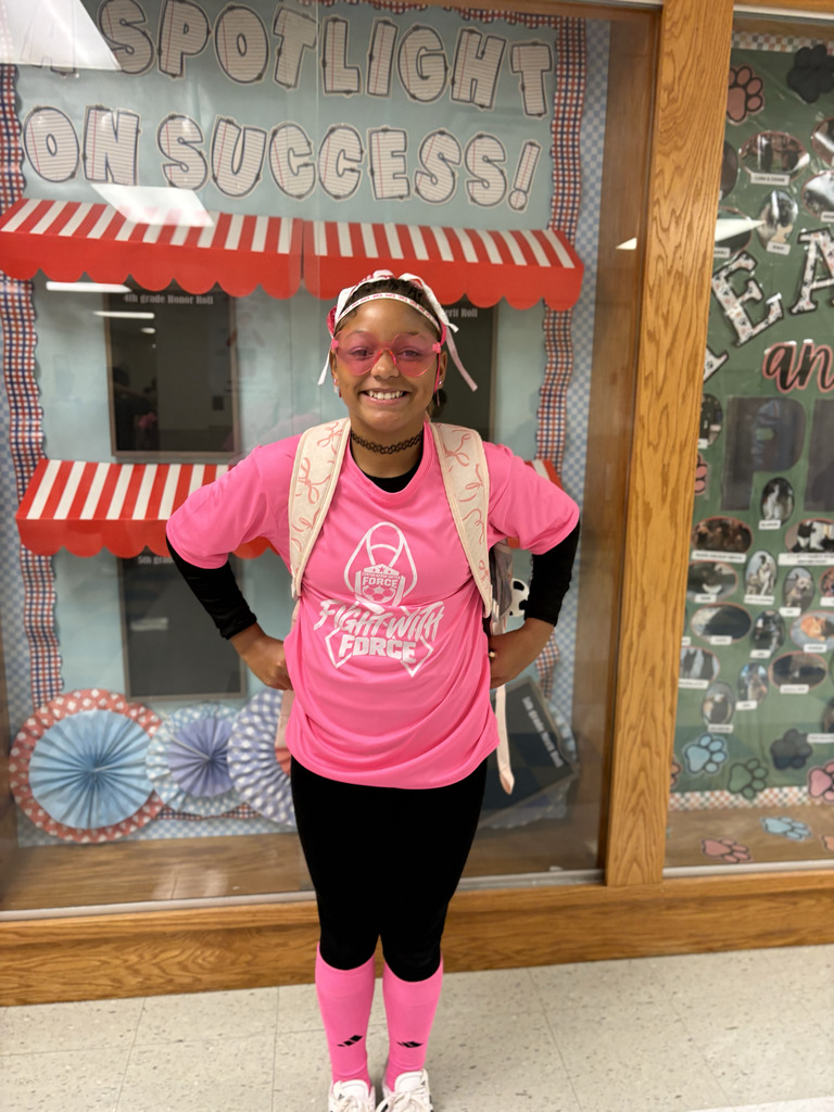 A student smiles in the hallway wearing a bright pink shirt, socks and glasses. 