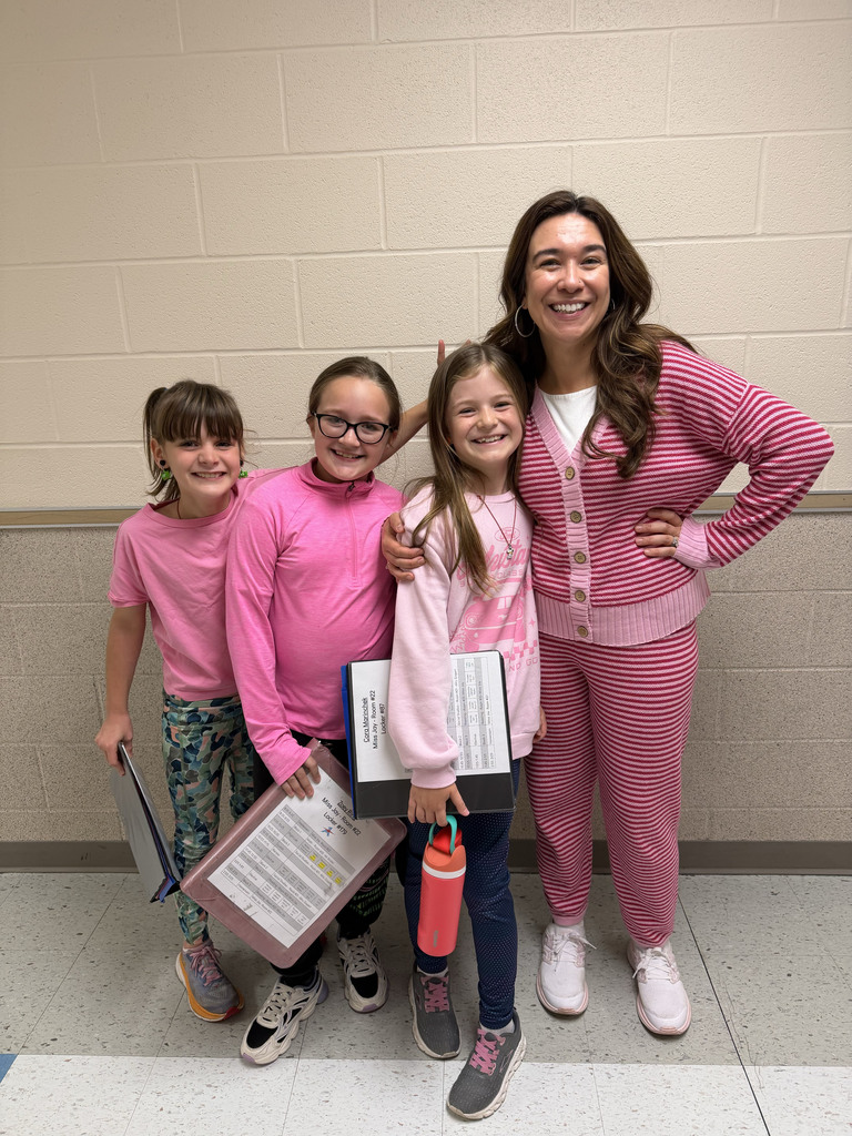 A teacher stands with three students in the hallway, all are wearing pink