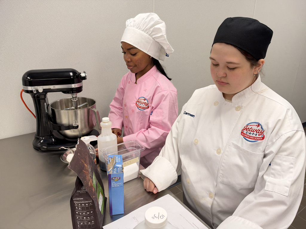 two students add ingredients to a stand mixer