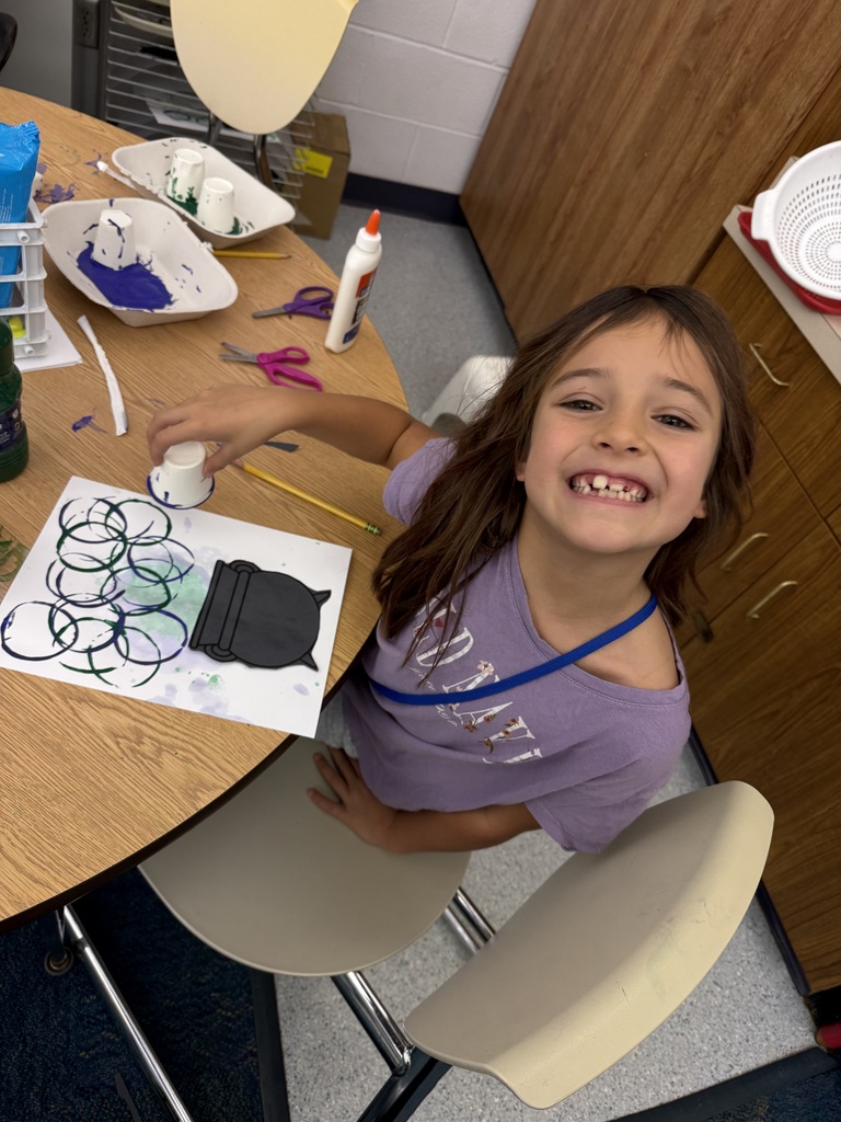 A student smiles while showing the drawing she made of the spooky soup