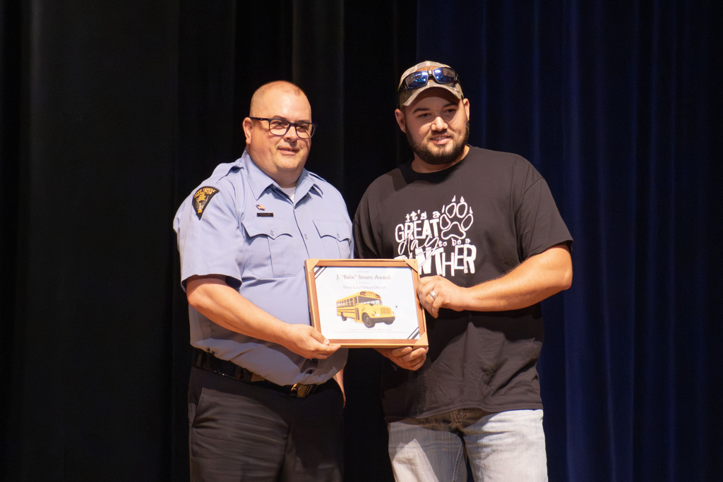 Two men stand together holding an award. One is from the state highway patrol and he is presenting the award