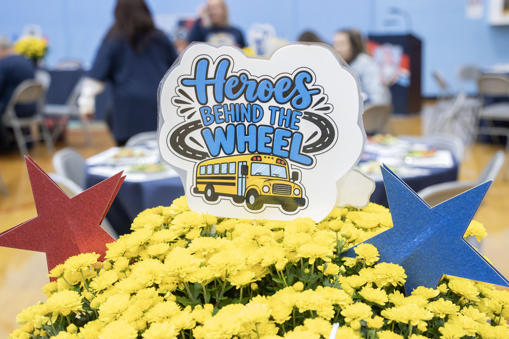 A picture with a pot of yellow mums and a sign that says "Heroes Behind the Wheel" along with a red and blue stars