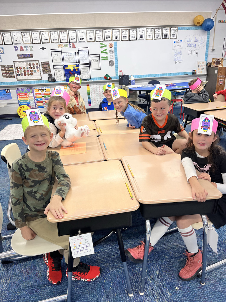 A group of seven students with colorful headbands sit at tables and smile for pictures