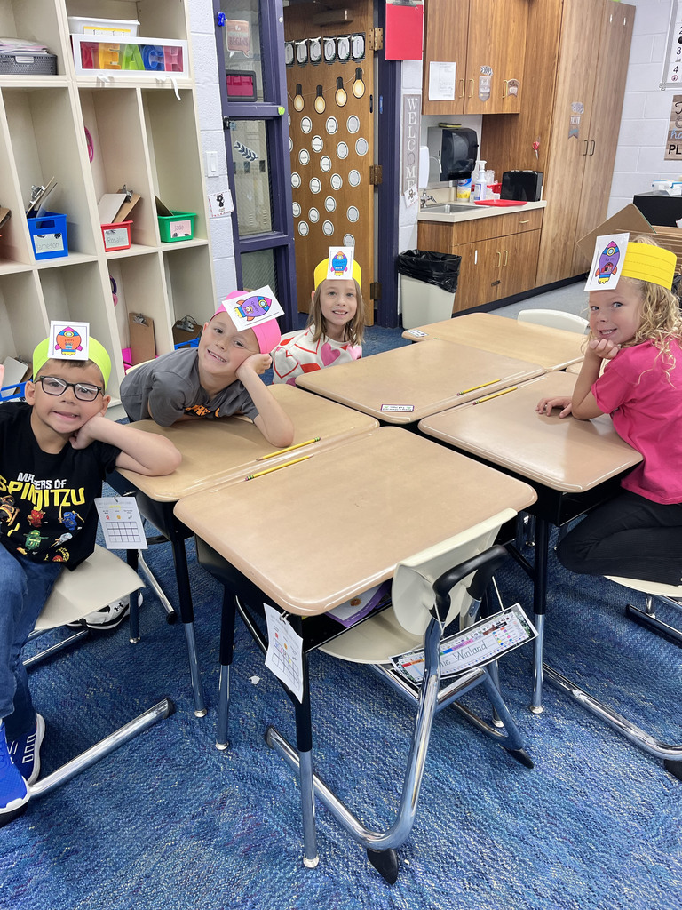 Four students wearing colorful headbands sit at tables and smile for pictures