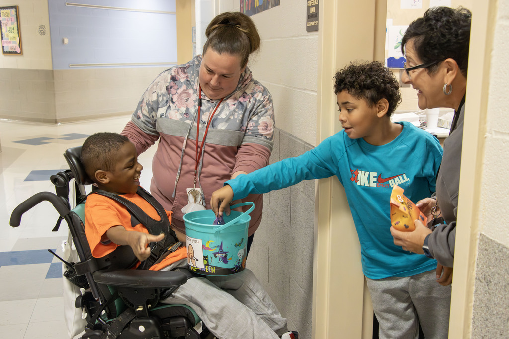 A student give candy to the trick or treaters while two staff members watch