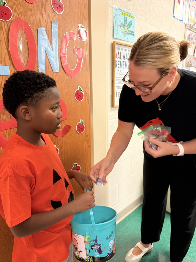 A students wearing an orange shirt gets candy from a teacher